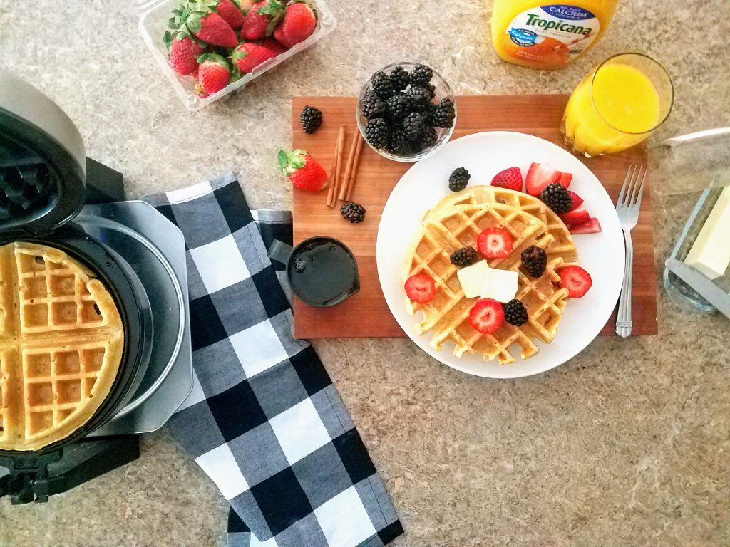 Waffles From Scratch on a plate with fresh fruit, real maple syrup and orange juice poured in a glass.